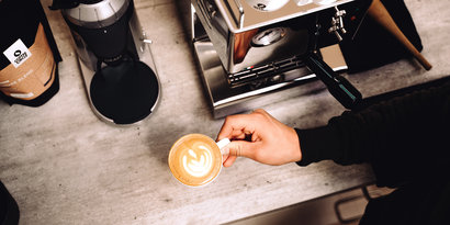 Eine Kaffeemühle, eine Espresso-Maschine und ein Cappuccino mit Latte-Art