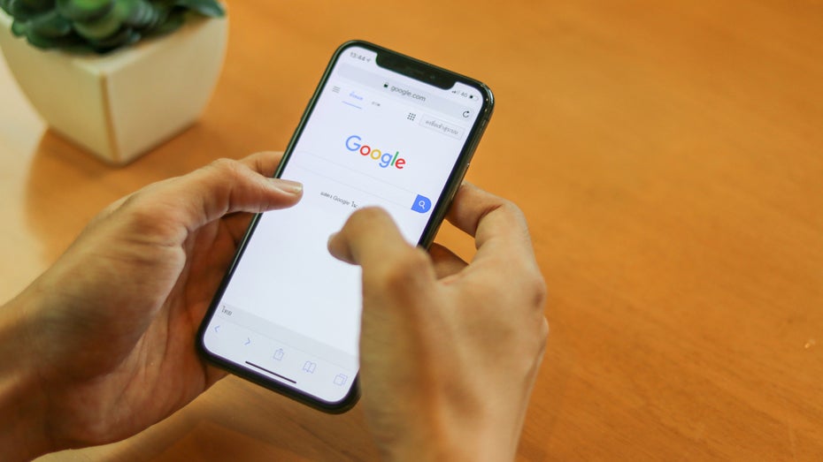 Zwei Hände halten ein Smartphone, auf welchem die Google-Suche geöffnet ist.