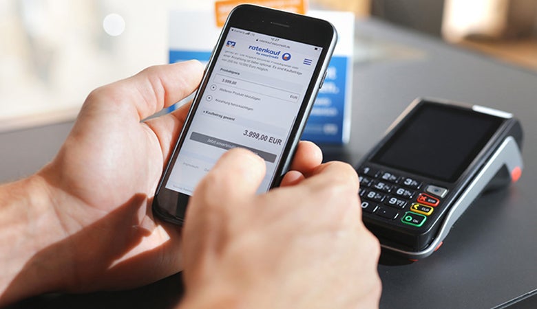 Das Bild zeigt eine Handyzahlung mit ratenkauf an der Ladenkasse. Im Hintergrund sieht man das Kartenterminal.