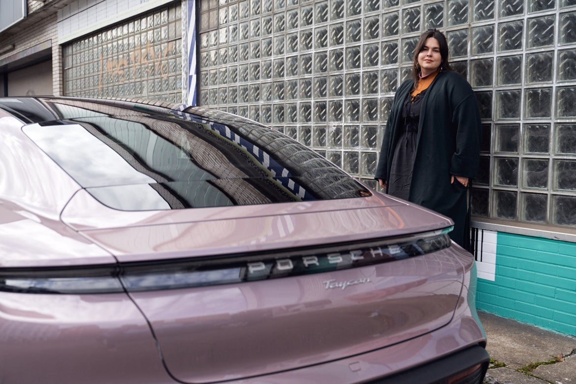Founder of the fashion leasing start-up Unown, Linda Ahrens, in front of a wall in the Affenfaust gallery in Hamburg. In front of it, the rear of a fully electric Porsche Taycan in the color