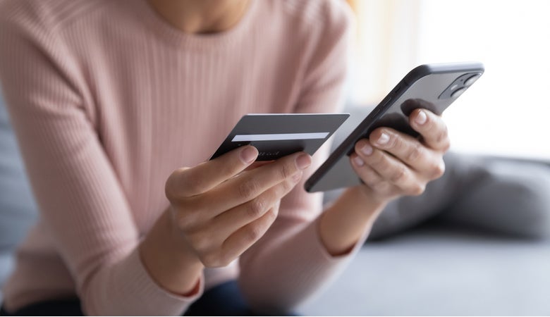 Auf dem Bild sieht man eine Frau, die eine schwarze Kreditkarte in der einen und ein iPhone in der anderen Hand hält.