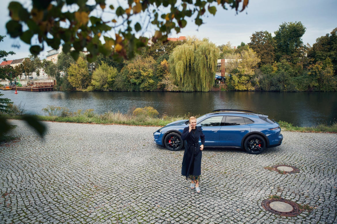 Victoria Reinsch entfernt sich telefonierend vom Porsche Taycan Cross Turismo, geparkt vor der Spree