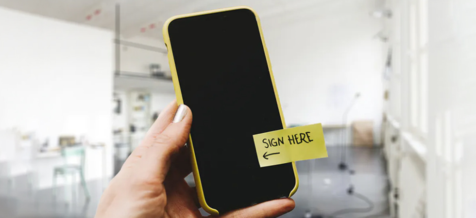 Auf dem Bild sieht man ein Smartphone auf dem ein "Sign-Here" Post-it steht. 