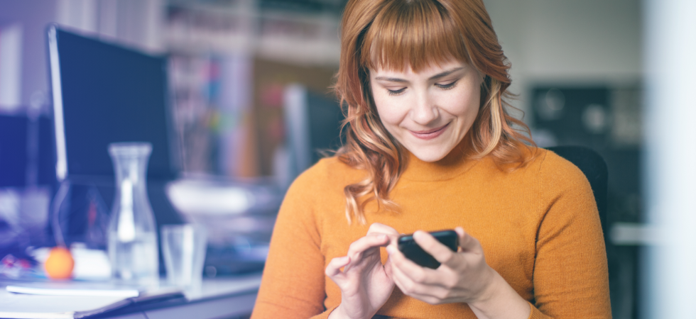 Eine Frau sitzt im Büro und schaut auf ihr Handy.