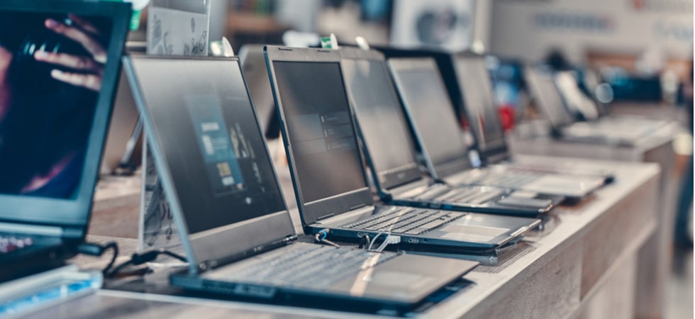 Eine Reihe von Laptops, aufgeklappt und auf einem Verkaufstresen innerhalb eines Technikhandels arrangiert