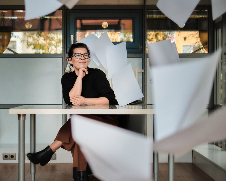 Sabrina Schultjan von Suchhelden am Schreibtisch, umgeben von fliegenden Papieren