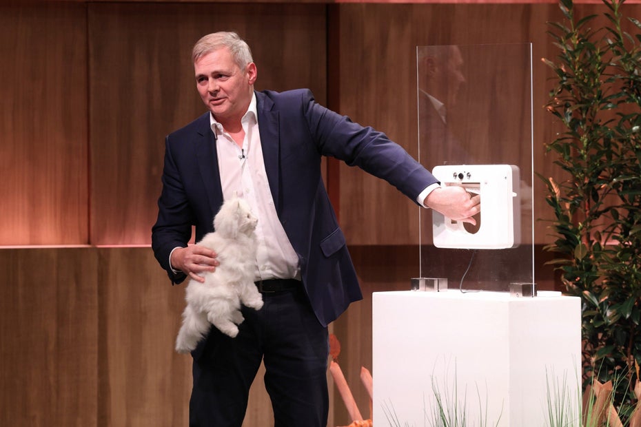 Ein Mann im Anzug führt eine Katzenklappe mithilfe einer Stoffkatze vor