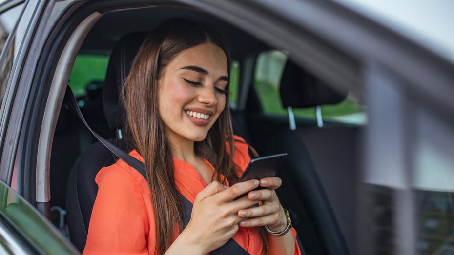 Eine Frau sitzt im Auto und benutzt ihr Smartphone (Symbolfoto: Shutterstock / Photoroyalty) Die Dating-App Hinge und das unmoralische Geschäft mit der Hoffnung