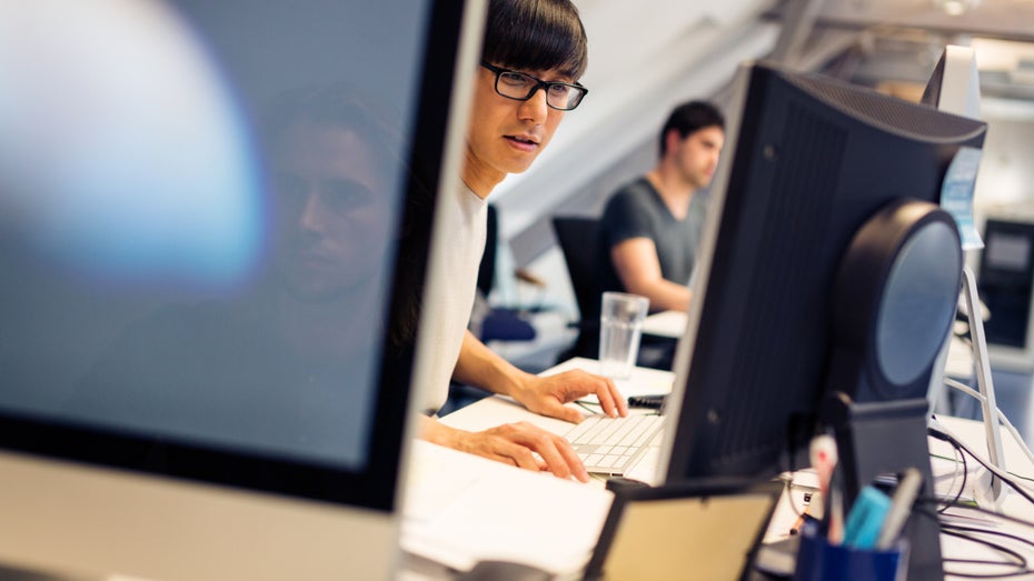 Junger Mann vor Computerbildschirmen (Symbolbild: Shutterstock / nullplus)