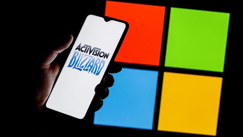 Smartphone mit dem Logo von Activision Blizzard vor dem Logo von Microsoft (Bild: Shutterstock / Sergei Elagin)