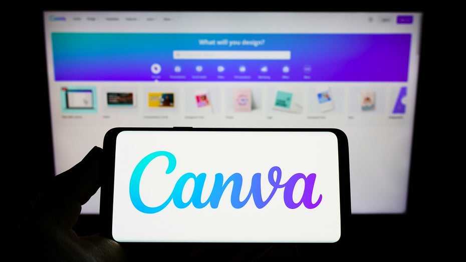 Canva-App auf einem Smartphone, dahinter Canva-Website auf einem Bildschirm (Bild: Shutterstock / T.Schneider)