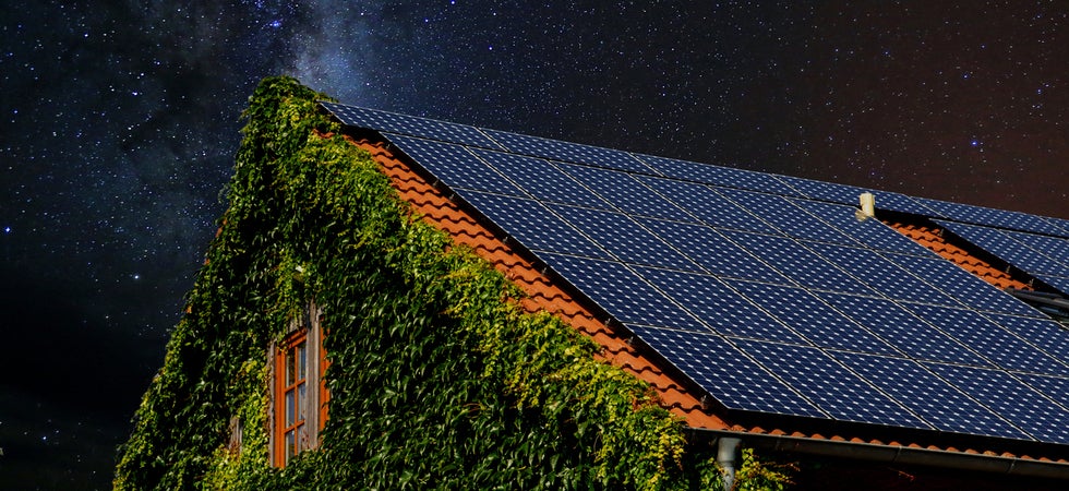 Ein mit Efeu bedektes Haus hat auf dem Dach Solarmodule. Der Sternenhimmel ist klar.