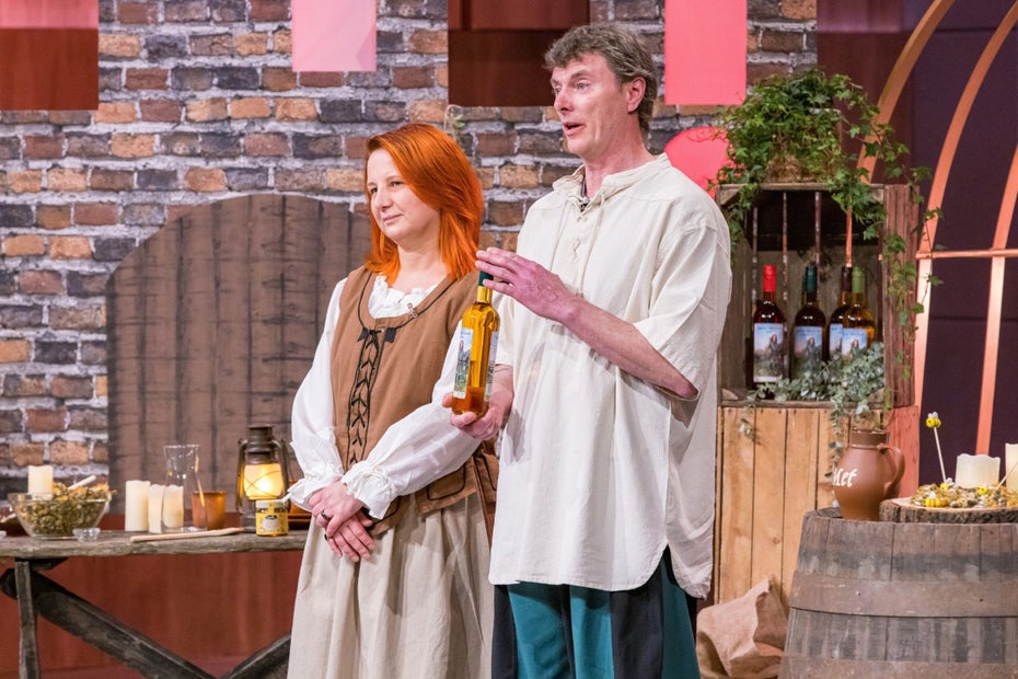 Ein Mann und eine Frau in mittelalterlicher Kleidung halten eine Flasche mit Honigwein und sprechen