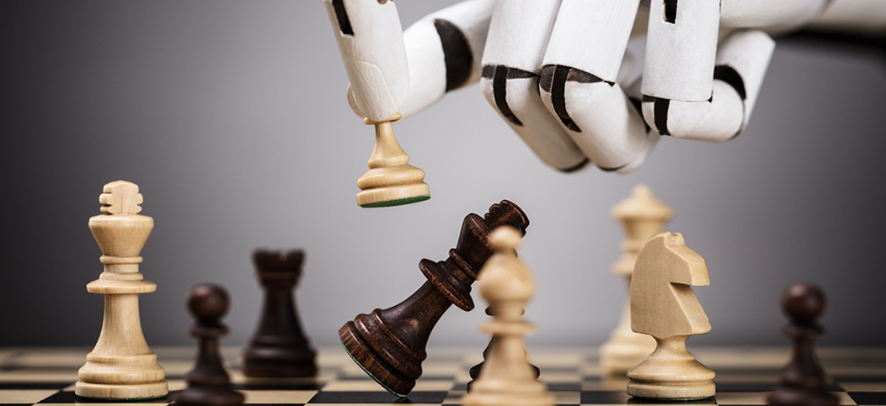Ein dekoratives Bild, welches eine Roboterhand zeigt, die Figuren auf einem Schachbrett bewegt. Damit soll ausgesagt werden, dass Strategien im Bereich Cybersecurity von Nöten sind.