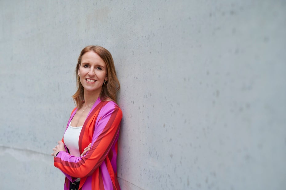 Verena Gründel wears a colorful blouse in front of a shimmering wall.