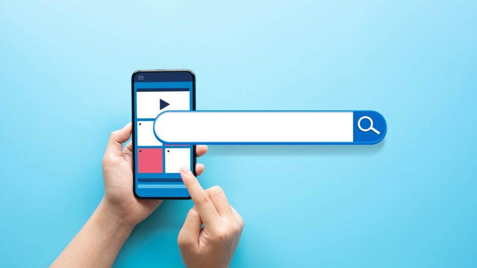 Suchmaschinen gibt es viele. Kann das Bezahlangebot Kagi mit Google und der KI-Suche von Perplexity mithalten? (Foto: Shutterstock / HAKINMHAN) Illustration einer Suchleiste, die über ein Handy übergelagert ist, das von einer Hand gehalten wird