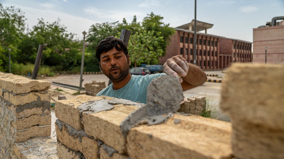Ein Maurer vermörtelt Blöcke aus Zuckerrohrabfällen. Die Wand ist heute Teil eines neuen Schulgebäudes bei Neu-Delhi. (Bild: UEL) Innovativer Schulbau: Zuckerrohrabfälle als nachhaltiger Baustoff