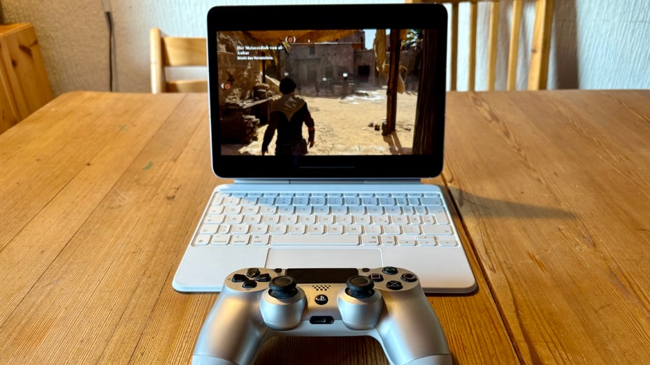 Ein iPad steht in einer Tasaturhülle auf einem Tisch. Davor liegt ein Playstation-Controller.